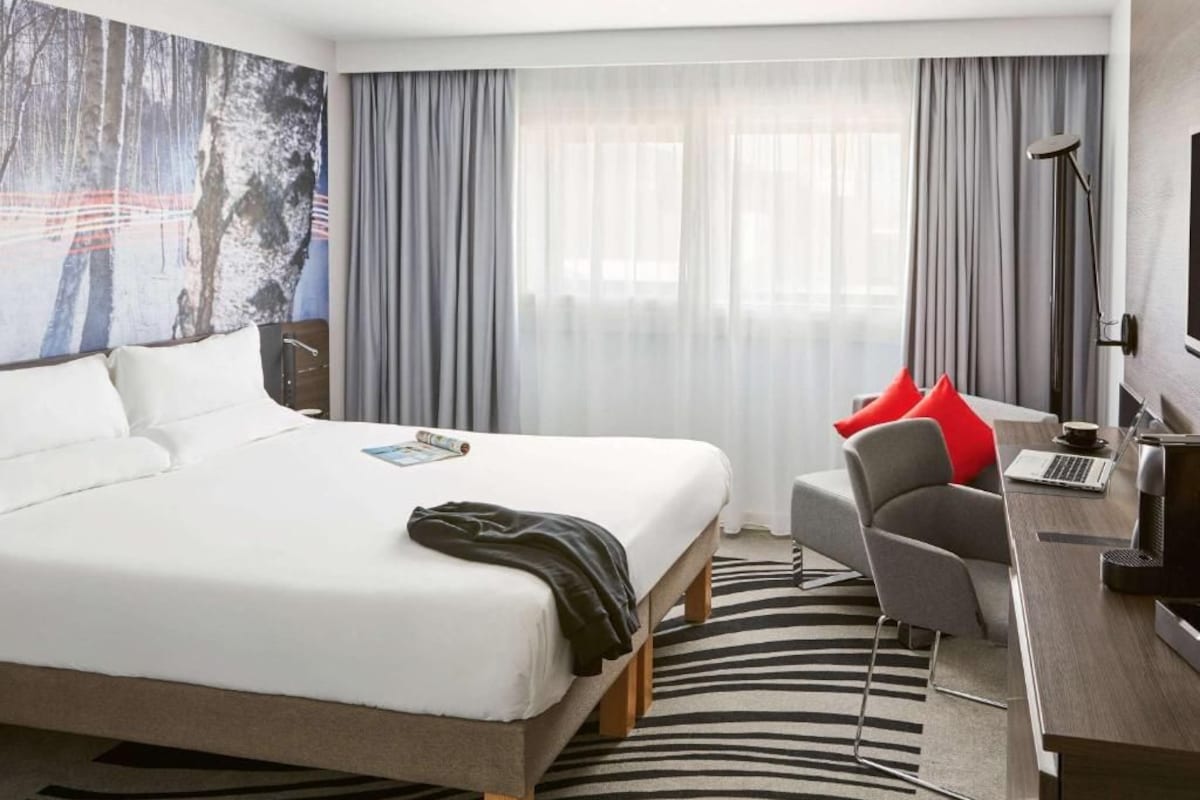 A hotel room with a large bed, a desk with a laptop, a chair, and a large painting on the wall.