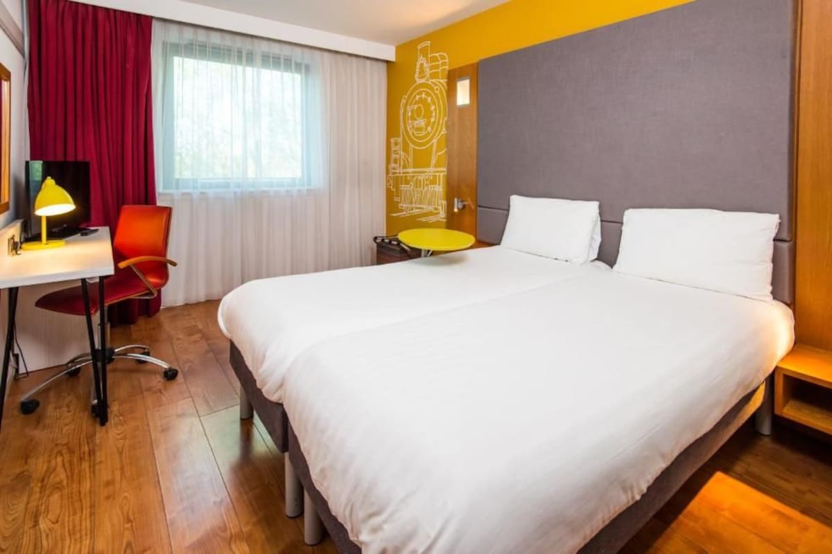 A hotel room with a bed, desk, chair, and a small round table.