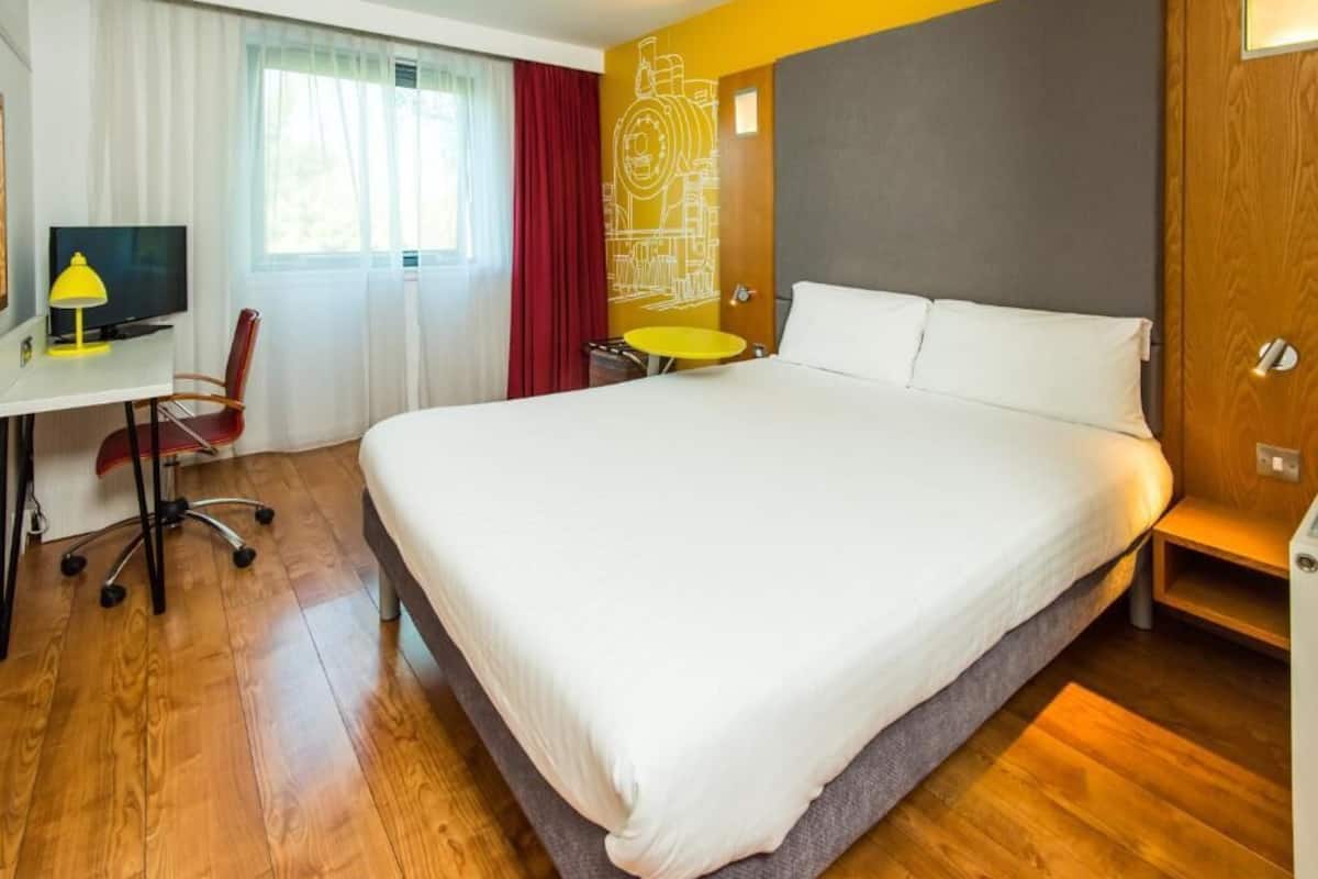 A hotel room with a large bed, a desk with a chair, a small round table, and a television.