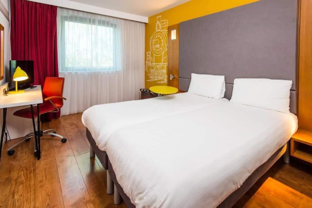 A hotel room with a bed, desk, chair, and a small round table.