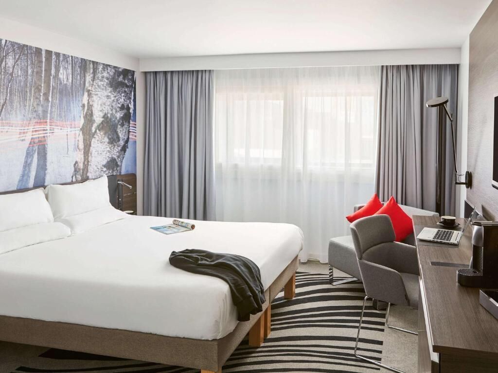 A hotel room with a large bed, a desk with a laptop, a chair, and a large painting on the wall.