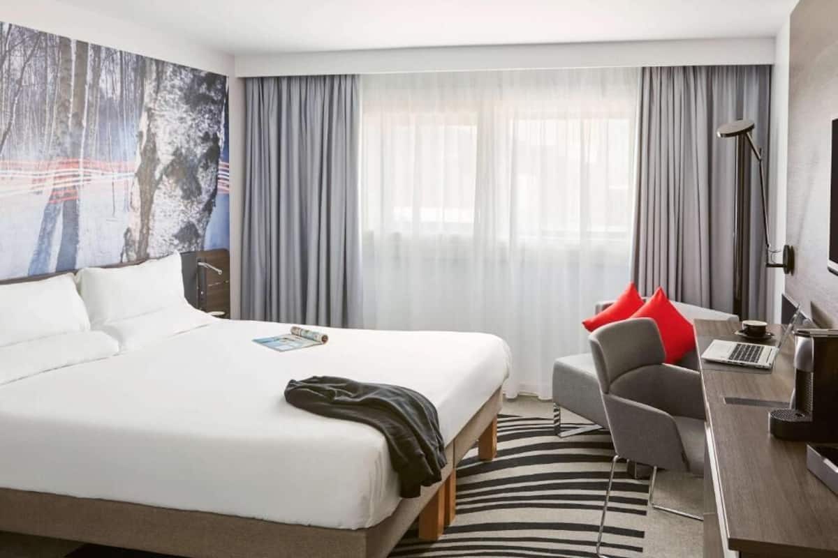 A hotel room with a large bed, a desk with a laptop, a chair, and a large painting on the wall.