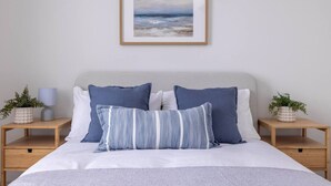 Un dormitorio con una cama, dos mesitas de noche, una lámpara y un cuadro en la pared.