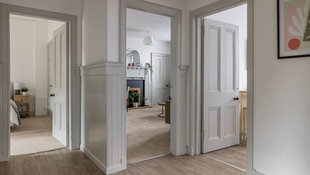 Un pasillo con puertas blancas que dan a varias habitaciones, una chimenea y una lámpara colgante.