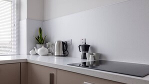 Una cocina moderna con encimera, hervidor, cafetera, tetera y una planta en maceta.
