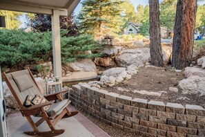 A patio area with a wooden rocking chair, a small table with a cup and saucer, and a brick retaining wall. - Minutes from NAU - 4 BR 3 BA sleeps 9 (Flagstaff)