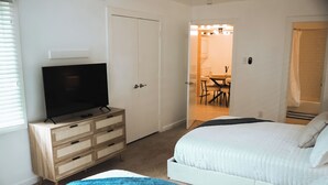 Een slaapkamer met een televisie, een houten dressoir, een bed en een badkamer met douchegordijn.