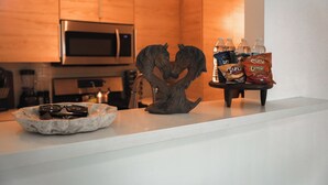 Een keuken met houten kasten, een magnetron en een koffieapparaat. Op het aanrecht staat een decoratief paardbeeldje en een schaal met zonnebrillen en chocolade.