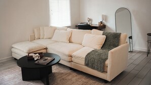Een moderne woonkamer met een beige hoekbank, een zwarte salontafel en een grote spiegel.