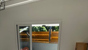 Un dormitorio con cama, una silla, un pequeño armario de madera y vista a un jacuzzi y un área de estar exterior a través de una puerta corrediza de vidrio.