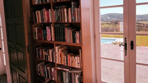 Ein Bücherregal voller Bücher, eine Holztür und ein Landschaftsblick durch eine Glastür.