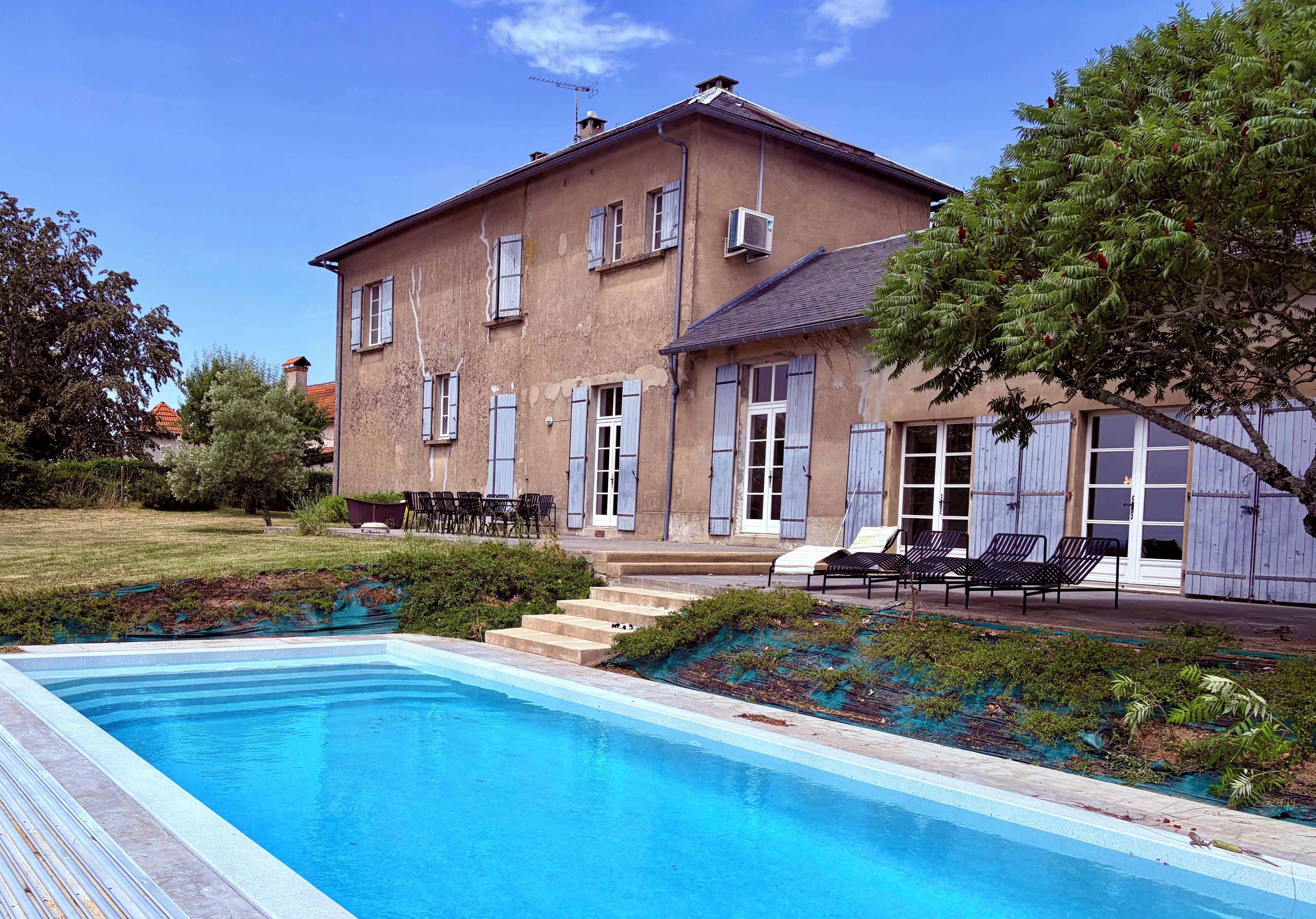 A two-story building with a swimming pool, outdoor seating, and a covered area with chairs.