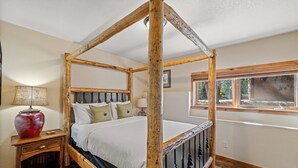 Una cama con dosel de madera, una mesita de noche con lámpara y una ventana con vistas al exterior.