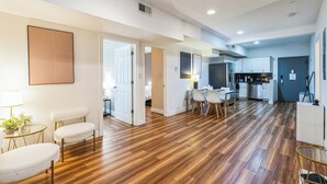 A spacious living area with a wooden floor, a dining table with chairs, a kitchen area, and a large window. - Elegant 2-bedroom apartment near Philadelphia Convention Center & Reading Market (Philadelphia)