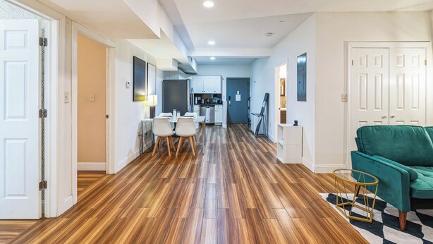A modern apartment with a wooden floor, a dining area with a table and chairs, a kitchen, and a green sofa. - Elegant 2-bedroom apartment near Philadelphia Convention Center & Reading Market (Philadelphia)