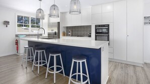 A modern kitchen with a central island, bar stools, stainless steel appliances, and pendant lighting. - 4 bed beautiful Ocean View Retreat (Bundeena)