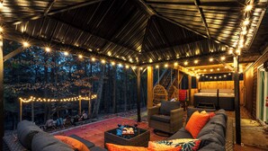 An outdoor patio with a covered seating area, string lights, and a hot tub.