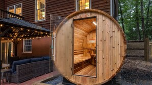 A wooden sauna structure with a bench inside, situated on a patio with outdoor seating and string lights.