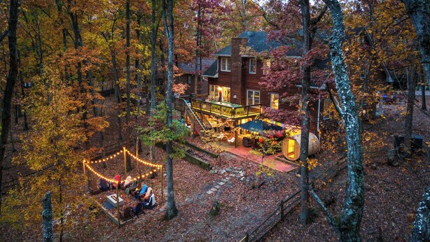 A rustic cabin surrounded by autumn foliage, featuring a deck, outdoor seating, and a fire pit.