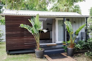 A small, single-story wooden building with a covered porch and a sliding glass door leading to a kitchen area. - Coastal Cabin Bundeena (Bundeena)