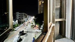 Une vue nocturne depuis une fenêtre d’hôtel, donnant sur une rue bordée de voitures garées et d’immeubles.