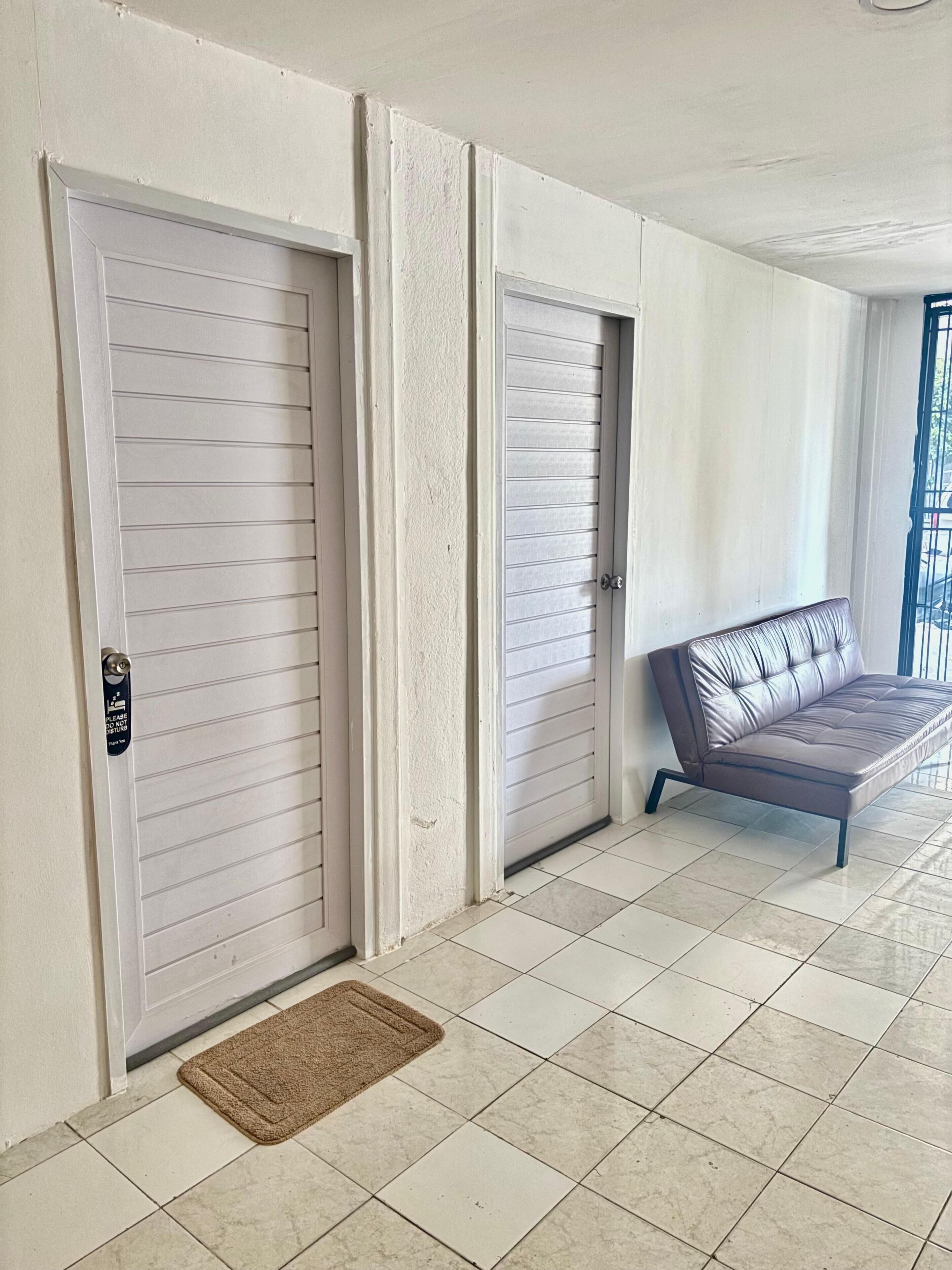 A hallway with two closed doors, a brown doormat, and a sofa in a corner.
