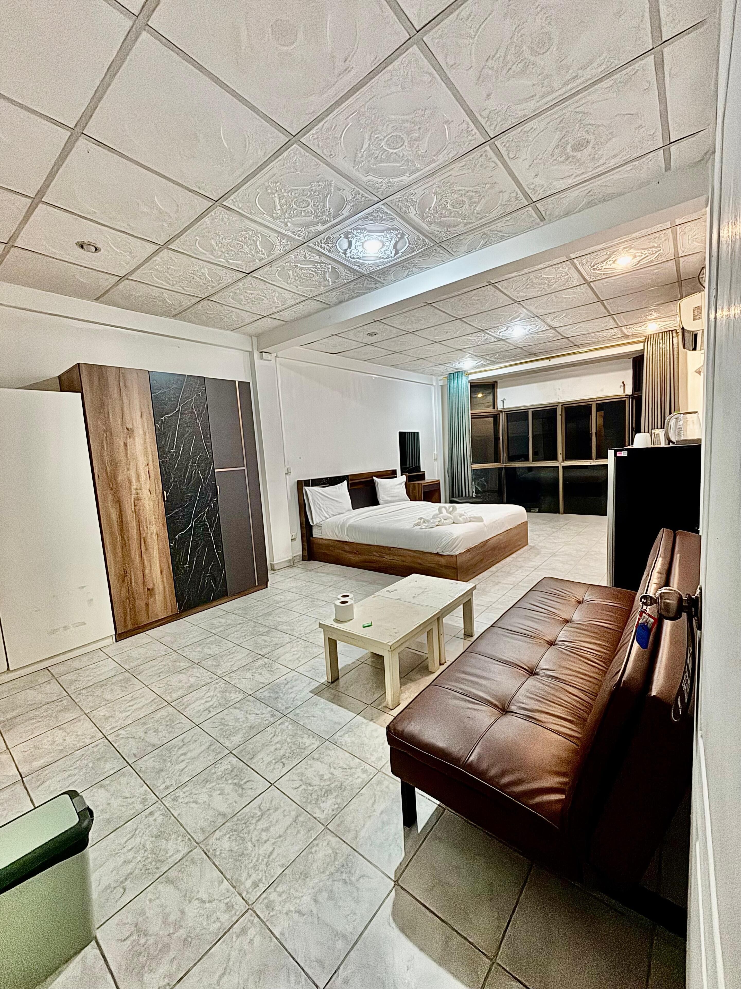 A spacious room with a large bed, a brown leather sofa, and a small table.
