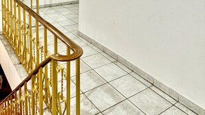 Un escalier avec une rampe dorée mène à un palier. Une fenêtre aux cadres en bois est visible au fond.
