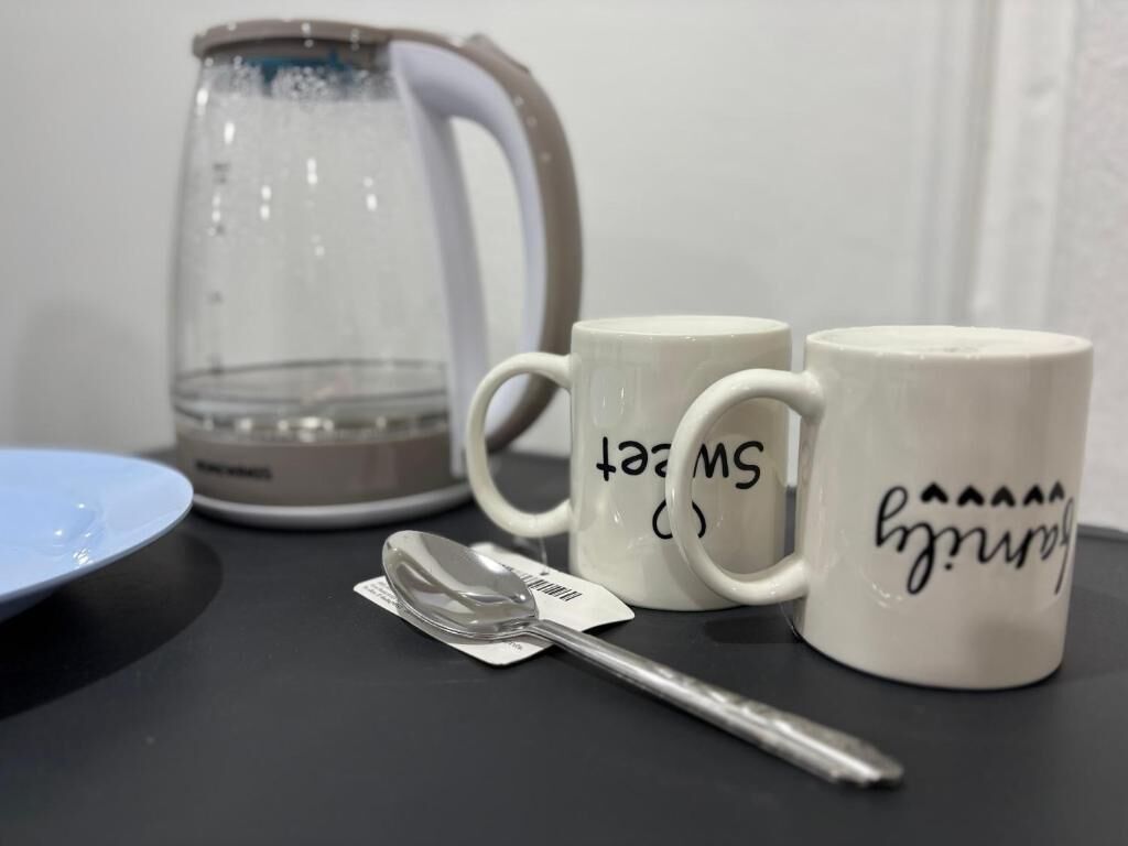 A table with a glass teapot, two white mugs with text, a spoon, and a blue plate.