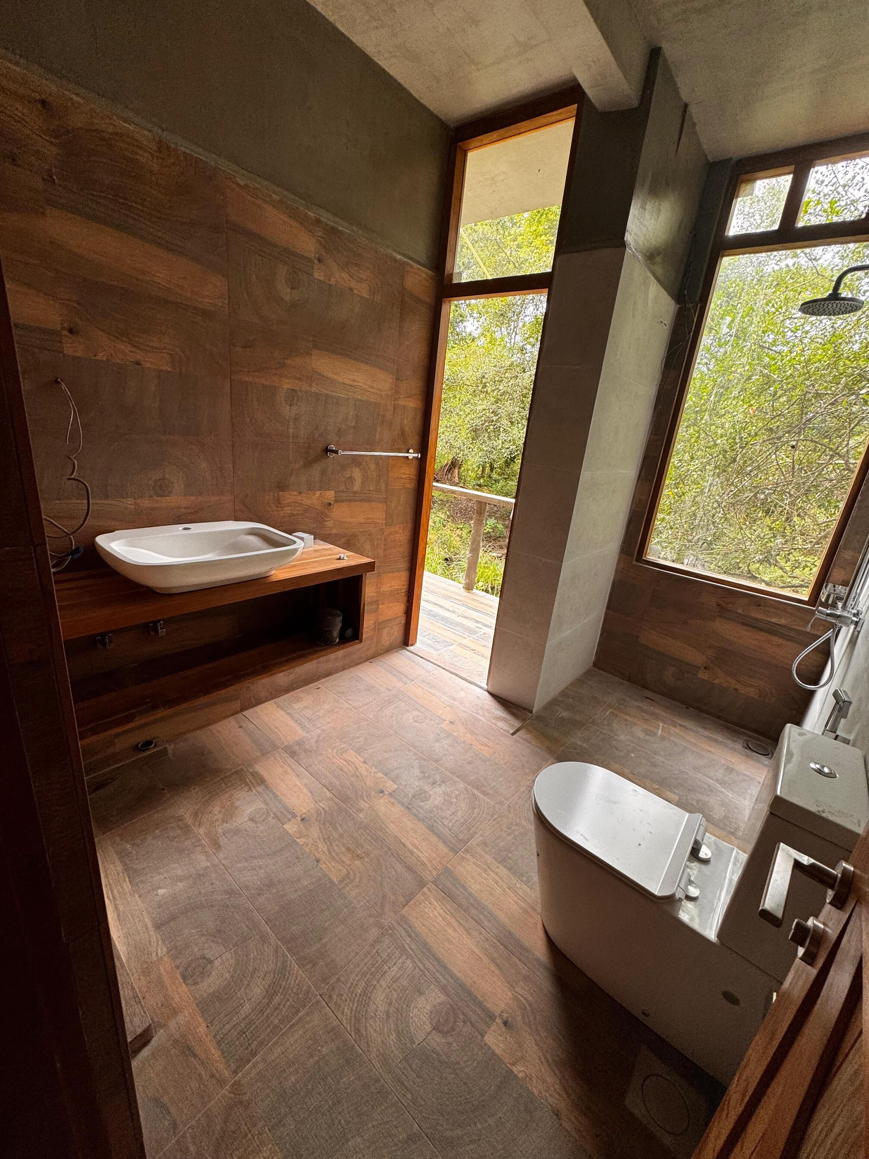 A modern bathroom with a freestanding bathtub, a wooden vanity, and a large window offering a view of greenery.