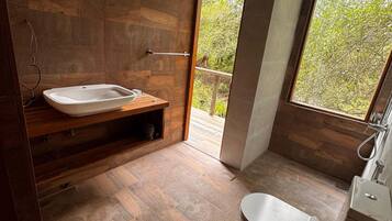 A modern bathroom with a freestanding bathtub, a wooden vanity, and a large window offering a view of greenery.