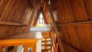 A wooden interior with a sloped ceiling, a wooden staircase, and a window at the top.