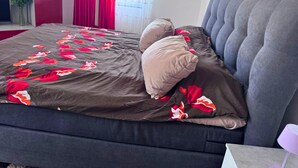 A bed with a floral bedspread, a grey upholstered headboard, and a vase of flowers on the nightstand. - Apartment in Danma mit Gemeinschaftskuche (Laubach)