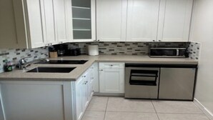 Una cocina compacta con gabinetes blancos, microondas, lavavajillas y salpicadero de azulejos.