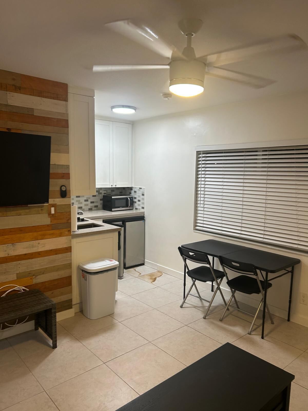 A compact kitchen with a microwave, sink, and a ceiling fan. There is a small dining area with a table and chairs.