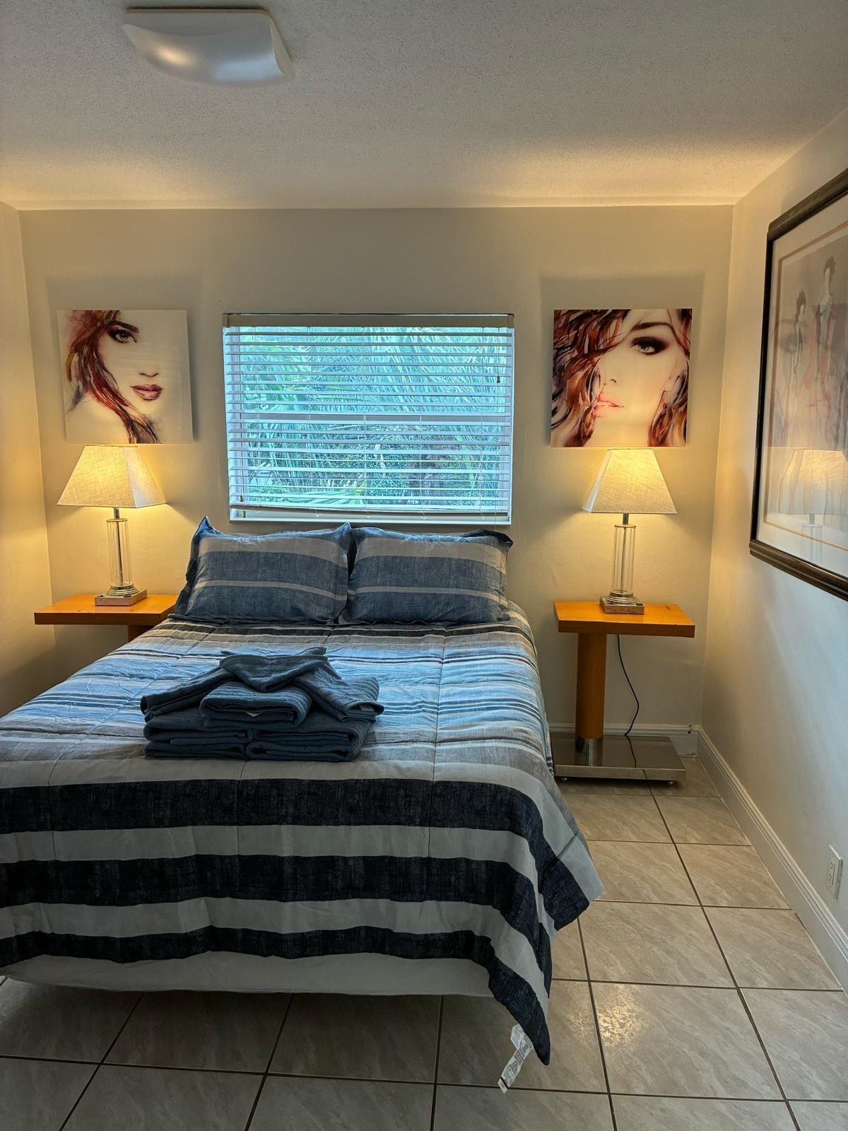 A neatly made bed with a striped bedspread, two bedside lamps, and artwork on the walls.