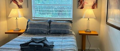 A neatly made bed with a striped bedspread, two bedside lamps, and artwork on the walls.
