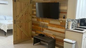 A modern kitchen with a flat-screen TV mounted on a wooden wall, a small bench, and a trash bin.