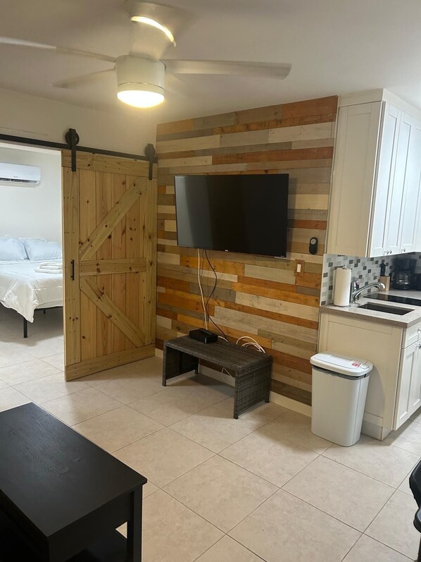A modern kitchen with a flat-screen TV mounted on a wooden wall, a small bench, and a trash bin.