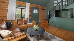 A cozy living room with a leather sofa, a round coffee table, and a staircase with a TV on the wall.