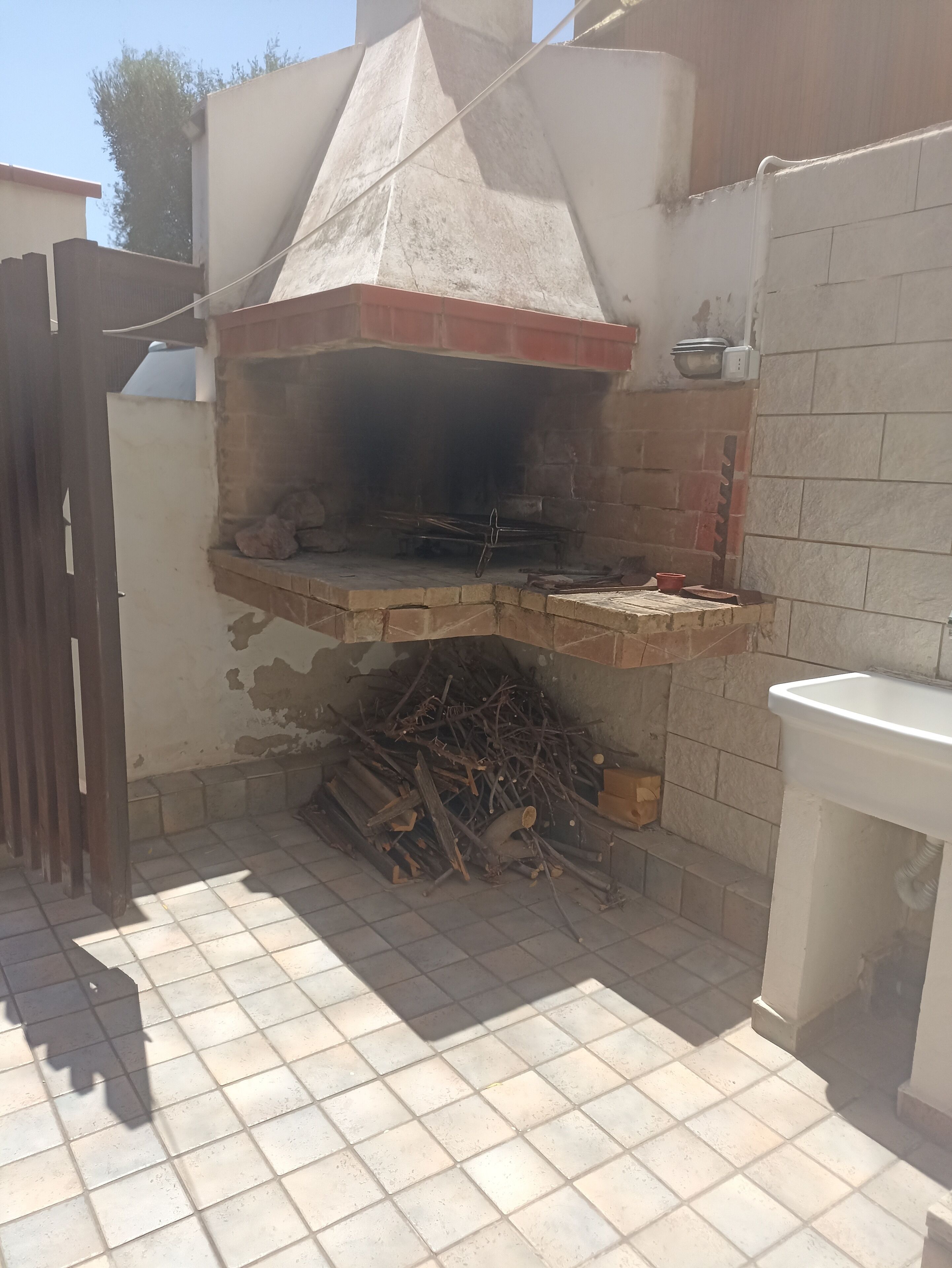 A brick-built outdoor oven with a chimney, a tiled floor, and a white sink nearby.