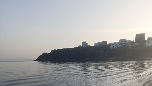 A beach with calm waters and a distant view of buildings on a hill.