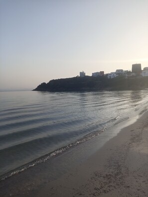 A beach with calm waters and a distant view of buildings on a hill. - Villa Vavu ideal for two families (Sardegna)