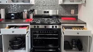 A compact kitchen with a stainless steel stove, an oven, and white cabinetry with open shelves. - Cityscape Retreat In Jersey City. Spacious apt for short and long term stay. (Jersey City)