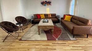 A living room with a brown sofa, two armchairs, a coffee table, and a colorful abstract painting on the wall. - Cityscape Retreat In Jersey City. Spacious apt for short and long term stay. (Jersey City)