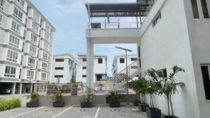Un pati pavimentat amb un edifici modern que té un passadís cobert i plantes en testos.
