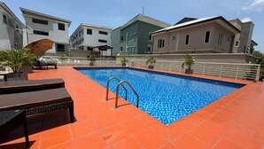Una piscina amb un solari de rajoles vermelles, envoltada d'edificis amb balcons i un cel serè.