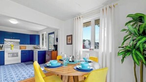 A modern kitchen with blue cabinets, a dining area with yellow chairs, and a large potted plant. - Waterview Retreat| Large Deck | Minutes to Downtown  (Charlottetown)