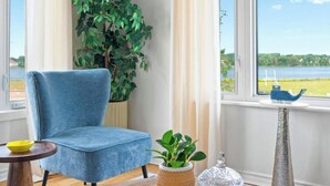 A room with a blue chair, a potted plant, a coffee table with a crystal vase, and a view of a lake through large windows. - Waterview Retreat| Large Deck | Minutes to Downtown  (Charlottetown)