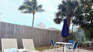 Un patio con sillones de descanso y una mesa, rodeado por una cerca de madera y palmeras.